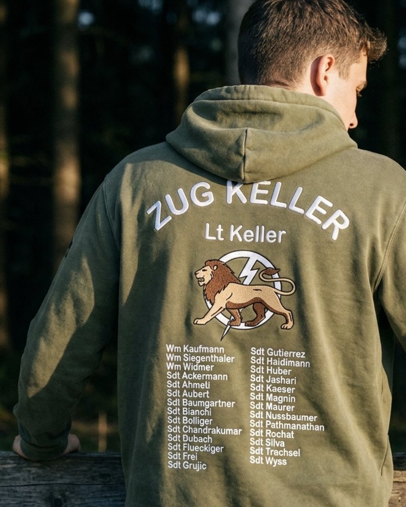 Rekrut im olivgrünen Hoodie «Zug Keller» mit Löwen-Motiv und Namensliste am Waldrand